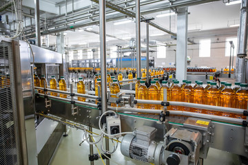 Conveyor belt or line in beverage plant with modern automated industrial machine equipment. Plastic PET bottles with fresh organic juice in factory interior
