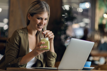 Happy woman using laptop while drinking smoothie in a cafe