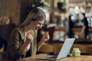 Happy businesswoman celebrating good news while using laptop in a cafe