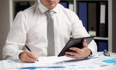 Businessman working with tablet pc, calculating, reading and writing reports. Office employee, table closeup. Business financial accounting concept.