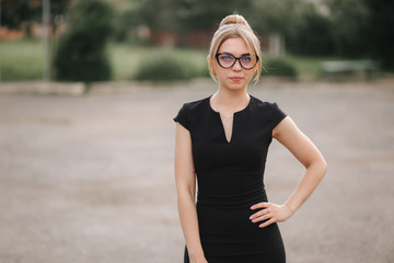 Young attractive female techer in black dress with sunglasses standing outside. Background of school