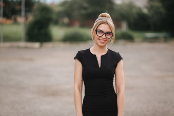 Young attractive female techer in black dress with sunglasses standing outside. Background of school