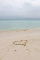 Fototapeta na wymiar The hand writing heart shaped on the beach by the sea with white waves and blue sky background