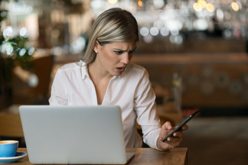 Young worried businesswoman text messaging on smart phone in a cafe