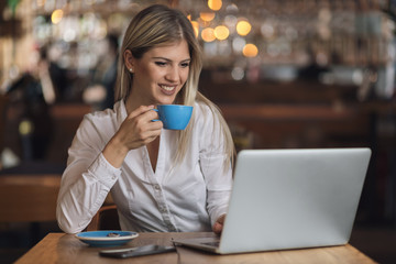 Young happy businesswoman reading an e-mail on laptop in a cafe