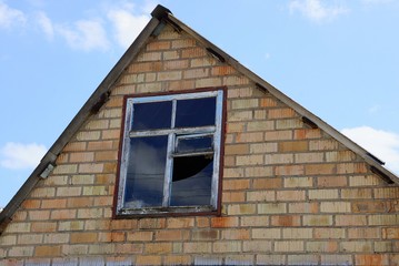 brown attic of a brick house with a broken window against a blue sky