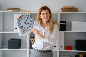 young beautiful blond woman in office hold clock in hands wait for end of working day