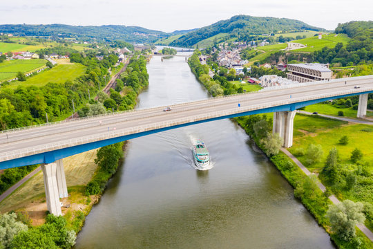 A leisure boat under high bridge where A13 motorway meets 8 highway over Moselle river. Aerial view of Schengen town center. Tripoint of borders of Luxembourg, Germany and France