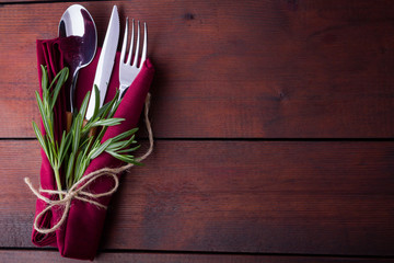 Set of cutlery knife, spoon, fork. Сutlery with burgundy napkin and twine. Rosemary on wooden background. Copy space. Top view
