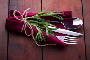 Set of cutlery knife, spoon, fork. Сutlery with burgundy napkin and twine. Rosemary on wooden background. Copy space. Top view