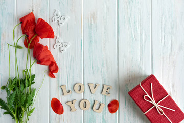 Photo of red poppies on a white wooden background with a gift and the words love you. The inscription love you and poppies flowers. View from above