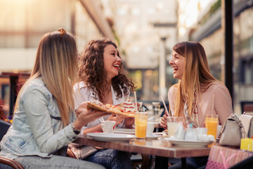 Three cheerful girls eating pizza in a outdoor restaurant