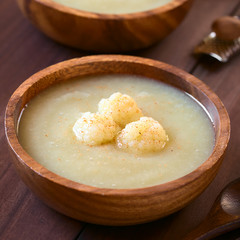 Cream of cauliflower soup in wooden bowl garnished with cauliflower florets and ground nutmeg, photographed with natural light (Selective Focus, Focus on the front of the cauliflower on the soup)