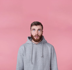 Portrait of young tired handsome guy looking up at the copy space, thinking about solving a problem, presents possible options, stands over pink background.