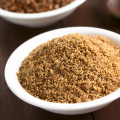 Ground or crushed brown flax seed or linseed in small bowl, photographed on dark wood with natural...