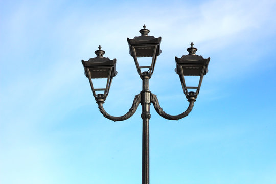photo of three modern metal LED lamps in vintage style on a single post against a blue sky