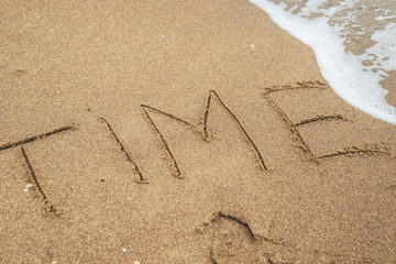 Time is the ultimate concept. The word Time written in the sand and disappearing under the influence of the sea wave.