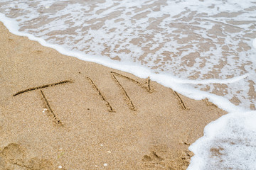 Time is the ultimate concept. The word Time written in the sand and disappearing under the influence of the sea wave.