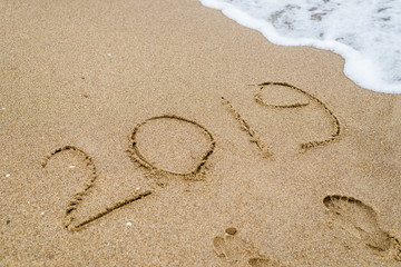 2019 inscription on sand washed away by the wave of the sea, ocean.