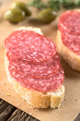 Salami slices on ciabatta bread with green olives in the back (Selective Focus, Focus on the front...