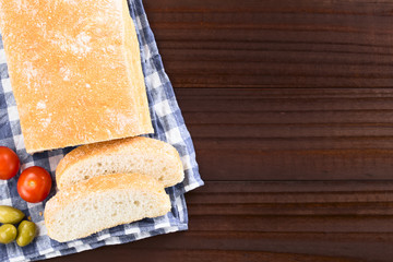 Fresh Italian ciabatta bread sliced, cherry tomatoes and green olives on the side, photographed overhead on dark wood (Selective Focus, Focus on the top of the bread)