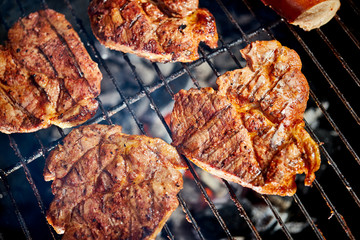 Juicy beef steaks on grill with flame on barbecue in the garden