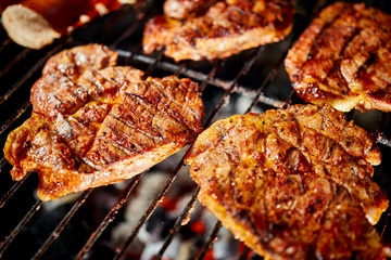 Juicy beef steaks on grill with flame on barbecue in the garden