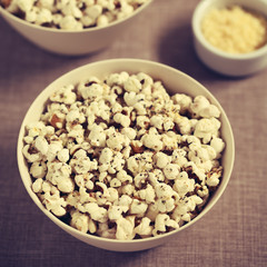 Homemade fresh savory popcorn with cheese, garlic and dried oregano in bowls, photographed with natural light (Selective Focus, Focus in the middle of the bowl) (Digitally Altered: Toned Image)