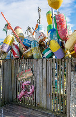 Fototapeta premium Lobstering in Provincetown sign on a weathered wood bench with many multi colored buoy floats behind