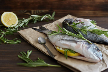 Fresh uncooked dorado or sea bream fish with lemon, herbs, oil, vegetables and spices on rustic...