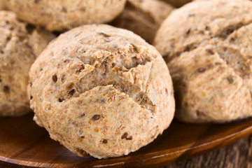 Fresh homemade wholegrain bread rolls with linseeds and sunflower seeds on wooden plate (Selective Focus, Focus on the front of the first bread roll)