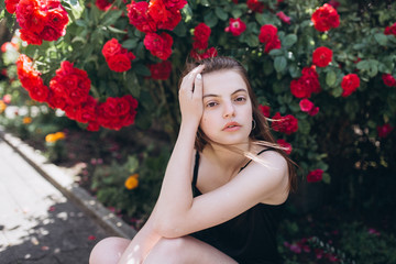 Obraz na płótnie Canvas Close up summer portrait of young sensual interesting pretty young woman outdoors near red roses. Modeling, fashion, trends, nature concept