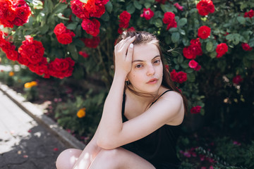 Obraz na płótnie Canvas Close up summer portrait of young sensual interesting pretty young woman outdoors near red roses. Modeling, fashion, trends, nature concept