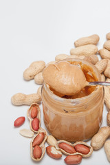 Creamy peanut butter in glass jar, peanut and spoon isolated on white background. A traditional product of American cuisine