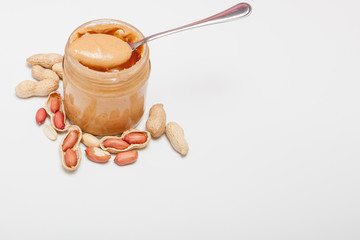 Creamy peanut butter in glass jar, peanut and spoon isolated on white background. A traditional product of American cuisine