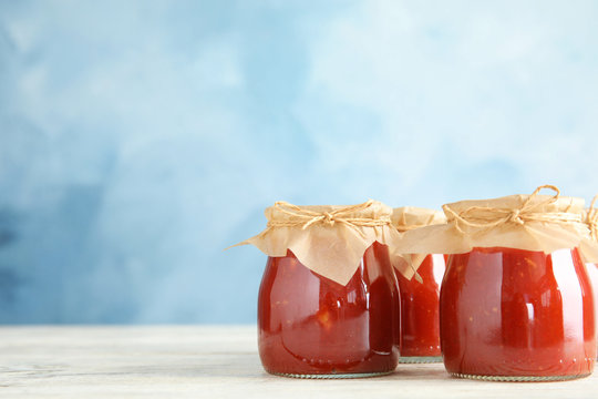 Jars of tomato sauce on wooden table against color background, space for text