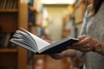 Woman holding open book in library, closeup