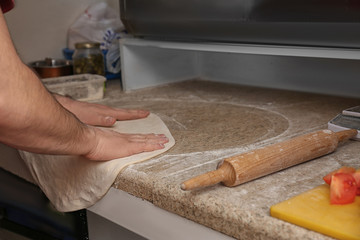 Man preparing dough for pizza at table, closeup. Oven recipe