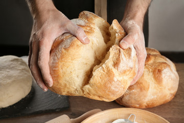 Male baker holding loaf of bread over table, closeup