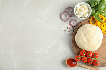 Flat lay composition with dough and ingredients for pizza on marble table, space for text