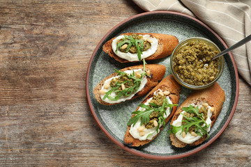 Plate with tasty bruschettas and pesto sauce on wooden table, top view. Space for text