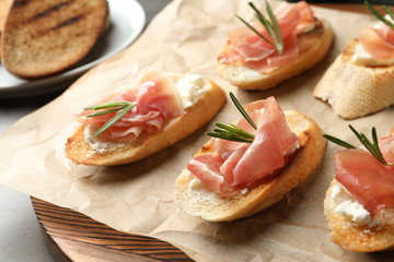 Tasty bruschettas with prosciutto and cream cheese on board, closeup
