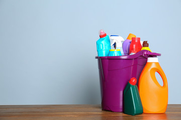 Plastic bucket with different cleaning products on table against color background. Space for text