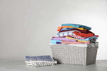 Wicker laundry basket with clean clothes on table against light background. Space for text