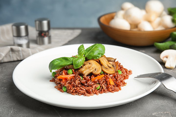 Plate of tasty brown rice with vegetables and mushrooms on grey table