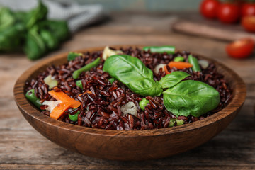 Plate of brown rice with vegetables on wooden table, closeup