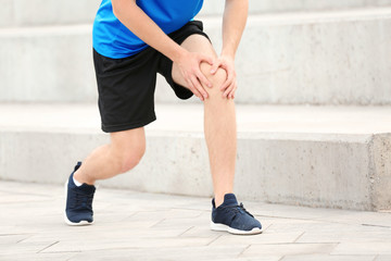 Fototapeta na wymiar Man in sportswear suffering from knee pain on stairs, closeup