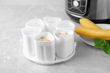 Cups of yogurt with bananas and multi cooker on table