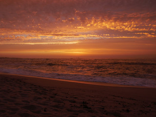 Fototapeta na wymiar Waves lapping on beach at sunset with beautiful orange sky in Portugal