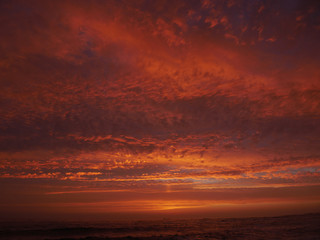 Vivid red sky at sunset on beach with dramatic clouds and dark sea